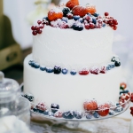 Pressebereich der Hochzeitsmesse HOCHZEITSTAGE, zweistöckige Hochzeitstorte mit Heidelbberen, Johannisbeeren, Himbeeren und ERdbeeren verziert und Puderzucker bestreut