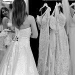 Pressebereich der Hochzeitsmesse HOCHZEITSTAGE, eine junge Frau probiert ihr Brautkleid an und betrachtet sich im Spiegel, mehrere weiße Brautkleider auf dem Bügel