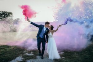 Hochzeitsanzug von Vesturo auf der Hochzeitsmesse München zu gewinnen Brautpaar mit farbigen Rauchfackeln in rot und blau